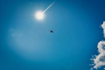 Silhouette of a helicopter against a blue sky with clouds