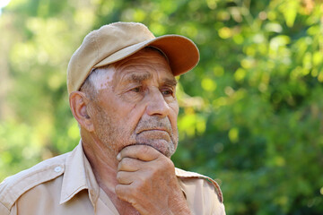 Portrait of pensive elderly man on green nature background. Concept of life in village, old age