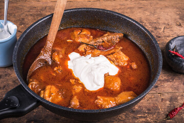 Cooking chicken paprikash, Hungarian stew in a skillet - adding sour cream to chicken stew with paprika.