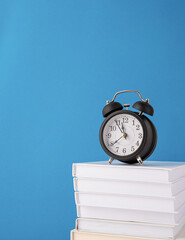 Black alarm clock on stack of books on blue background, mockup design