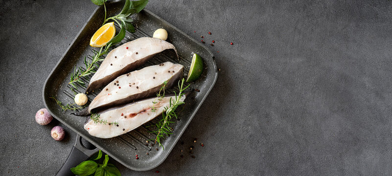 Raw halibut fish steaks with herbs and lemon prepared for cooking in a grill pan. Long banner with copy space. Healthy omega 3 unsaturated fats good for brain and mental clarity