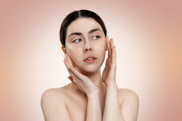 Portrait of a young beautiful woman holding her face with her hands, on which white arrows are applied. Beige background. Copy space. The concept of plastic surgery and rejuvenation