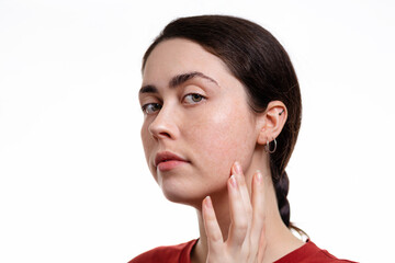 Close-up portrait of a young caucasian beautiful woman pointing at her skin. White background. Copy space. The concept of beauty and facial care