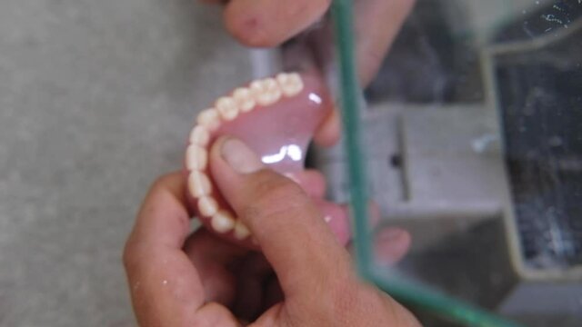 Dental technician holding artificial jaw mold with teeth and polishing them in the lab. Dentist brushing teeth with professional working tools