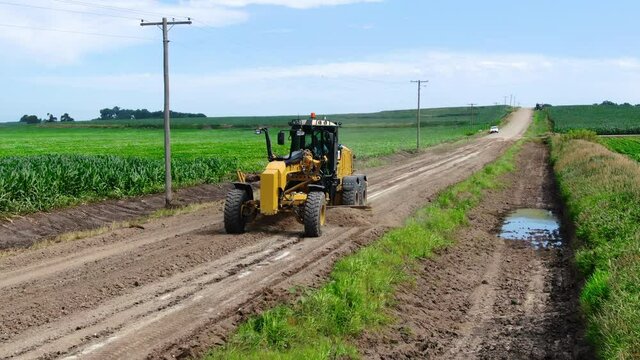 Road grader leveling gravel on road in rural landscape