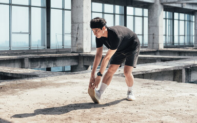 Young Asian man is doing leg stretching in an abandoned reinforced concrete building