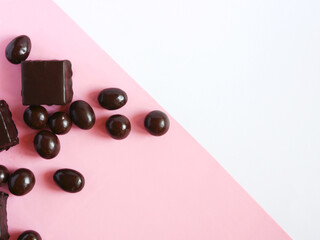 Square chocolate candies and nuts covered in chocolate on a pink and white background. Place for your text.