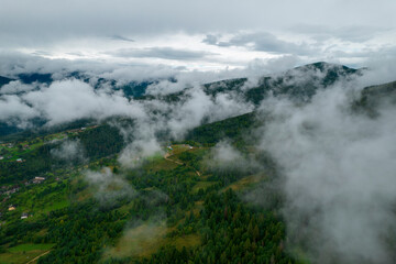 Rainy weather in mountains. Misty fog blowing over pine tree forest. Aerial footage of spruce forest trees on the mountain hills at misty day. Morning fog at beautiful summer forest.