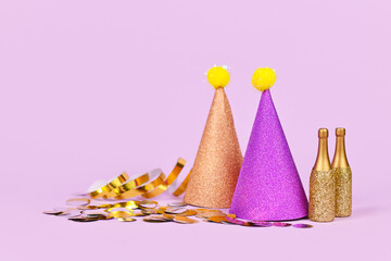 Glittering party hat, small golden champagne bottles and party streamers on violet background with copy space