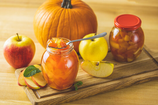 Fresh homemade pumpkin apple marmalade jam in glass jar on a wooden background. Several fresh apples, pumpkin and mint are near it