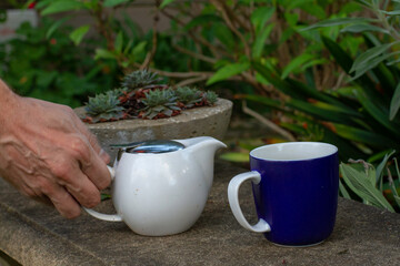 Man with strong hands about to pour tea into cup
