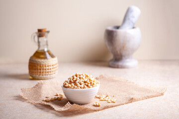 Pine nuts in a bowl on a jute napkin, cedar oil in a jug, pestle and mortar