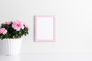 Pink frame mockup on white wall with pink flowers in pot decoration. Front view