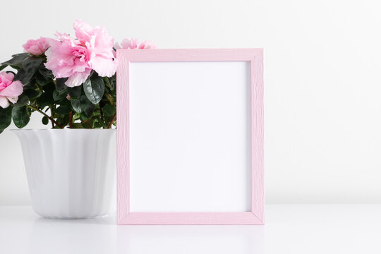 Pink frame mockup on white wall with pink flowers in pot decoration. Front view