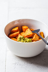 Baked sweet potato wedges with basil pesto in white bowl. Healthy vegan food concept.