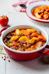 Beef stew with potatoes and carrots in tomato sauce in red pot, gray  background.