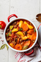 Beef stew with potatoes and carrots in tomato sauce in red pot, gray  background.