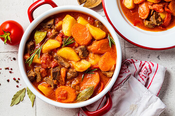 Beef stew with potatoes and carrots in tomato sauce in red pot, gray  background.
