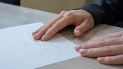 Close-up woman reads the text to the blind. Woman's hands on paper with braille code.