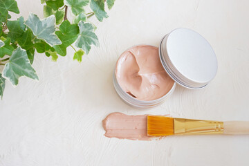 cosmetic brush, open jar with pink clay on light textured background
