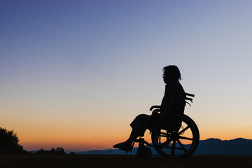 Obraz premium Silhouette Disabled handicapped man is sitting on wheelchair at sunset.