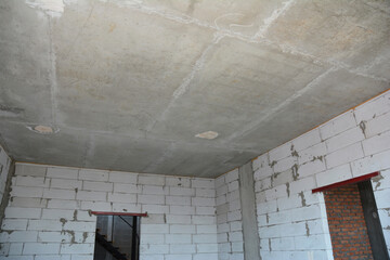 An inside view of an empty room of the house under construction with brick walls without finishing,  metal door lintels of two doorways and concrete slab ceiling.