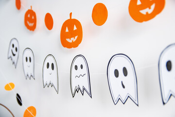 Festive decor on the white wall garland paper in the form of a pumpkin, ghost. Halloween holiday decor.