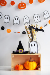 Halloween Concept. Festive decor on a white background: green phanar, crocheted pumpkins, cocktail straws, gifts.
