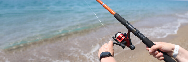 Man spins line on reel of fishing rod at sea