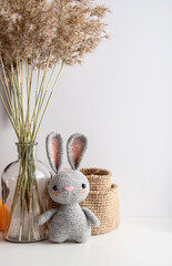 Cozy decor of the house handmade crocheted bunny, jute basket, glass vase with a bouquet of dry ears on a white background with space for copying.