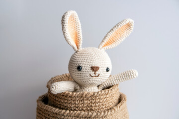 Crocheted bunny sits in a jute basket on a white background.