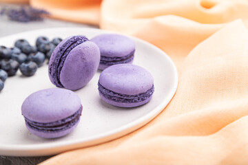 Obraz na płótnie Canvas Purple macarons or macaroons cakes with blueberries on white ceramic plate on a gray concrete background. Side view, selective focus.
