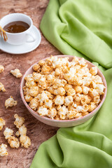 Popcorn with caramel in ceramic bowl on brown concrete background. Side view.