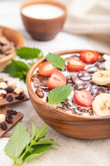Chocolate cornflakes with milk and strawberry in wooden bowl on white wooden background. Side view, selective focus.