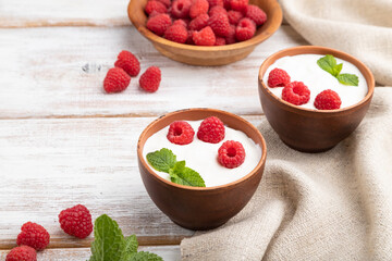 Yogurt with raspberry in clay cups on white wooden background. Side view.