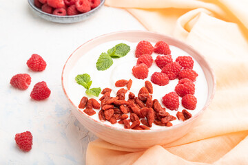 Yogurt with raspberry and goji berries in ceramic bowl on white concrete background. Side view.