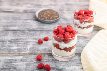 Yogurt with raspberry, goji berries and chia seeds in glass on gray wooden background. Side view, selective focus.