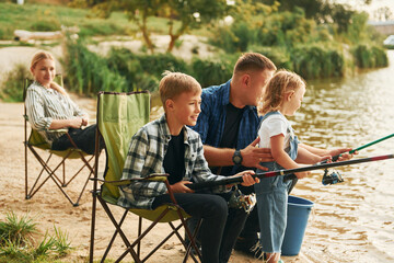 Fototapeta premium Positive emotions. Father and mother with son and daughter on fishing together outdoors at summertime