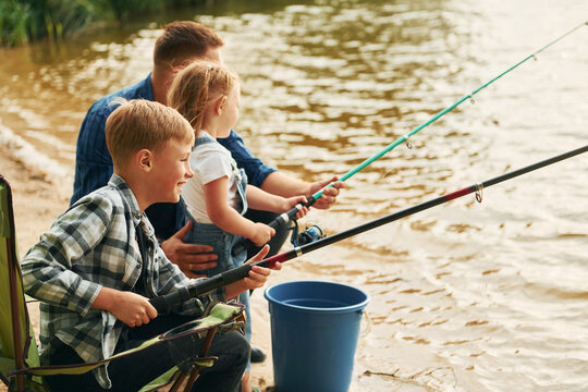 Sitting together. Father with son and daughter on fishing outdoors at summertime