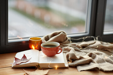 season, leisure and objects concept - cup of coffee, book, autumn leaves and candle on window sill at home