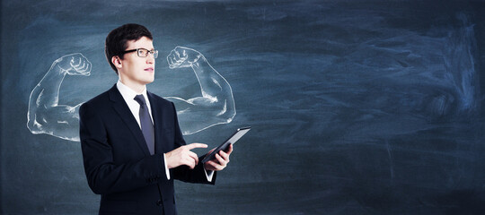 Attractive young european businessman with strong biceps arms sketch using tablet on blackboard...