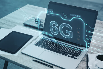 Close up of wooden desktop with laptop and other items, creative 6G chip hologram on blurry background. Wireless information and future concept. Double exposure.