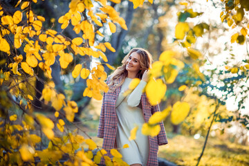 Outdoor autumn portrait of young beautiful woman in trendy outfit. Smiling girl with gorgeous blond hair. Fashionable warm plaid coat, knitted white dress.