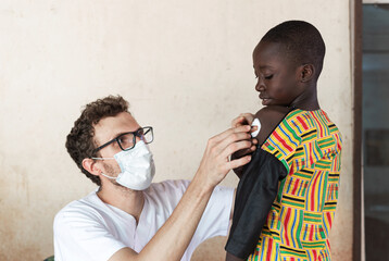 White doctor with face mask and glasses, putting a cotton ball on the injection site on the arm of...