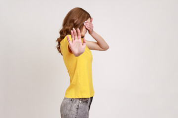 I'm not watching! Profile portrait of scared shamed teenager girl in casual yellow T-shirt covering...