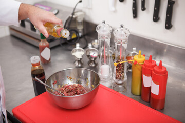 Chef adding oil to chopped beef for tartar