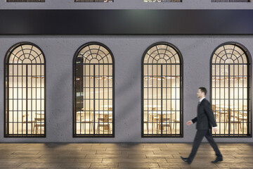 Businessman walking past creative business center exterior with windows and shadows at night.