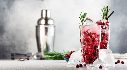 Cranberry cocktail with vodka, ice, juice, rosemary and red berries in highball glass. Refreshing long drink. Gray table background with negative space