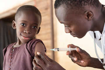 Cute little black African boy looking at camera during routine vaccination; childhood disease...