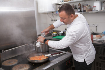 Chef salting frying vegetables in the pan, copy space